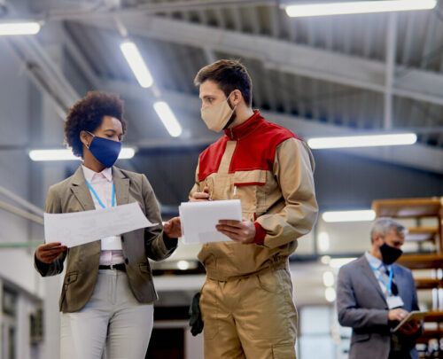 Woodworking factory laborer communicating with female company manager at production facility during coronavirus pandemic.