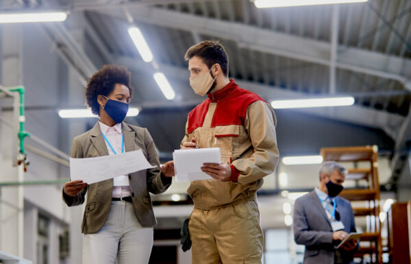 Woodworking factory laborer communicating with female company manager at production facility during coronavirus pandemic.